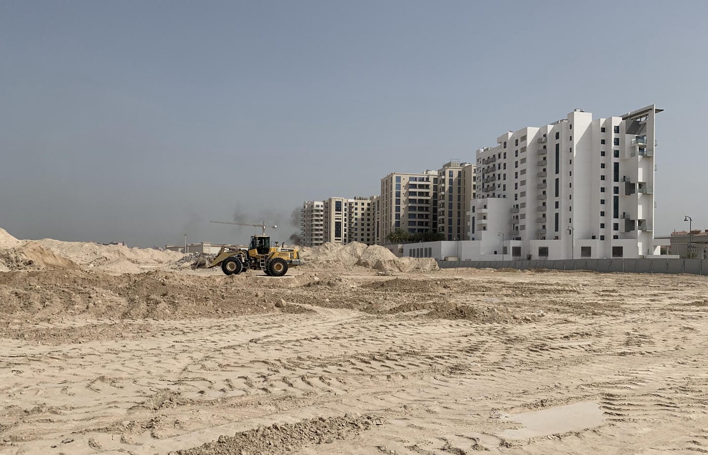 Wheel loader at cleared site with Dubai buildings in background