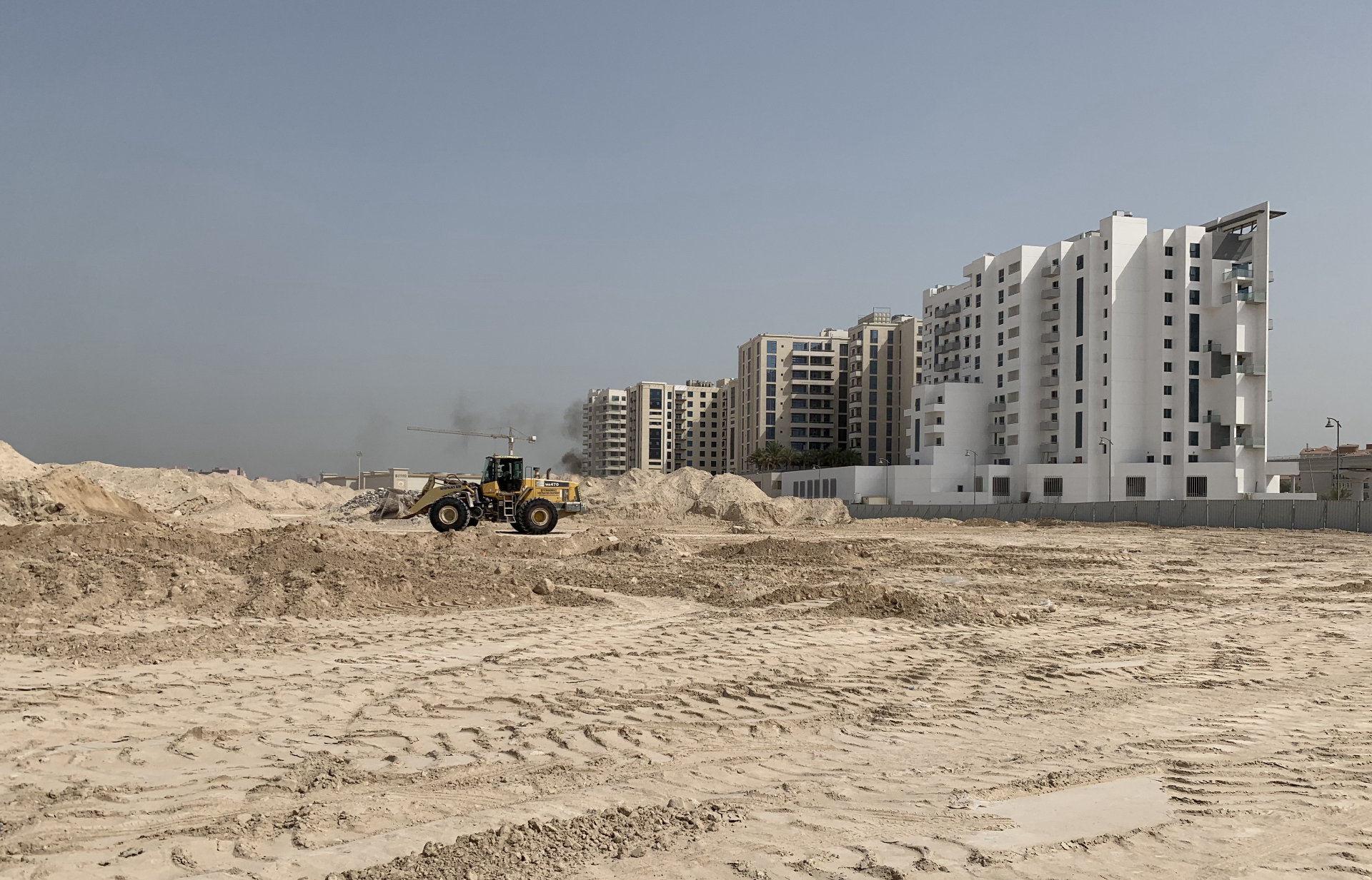 Wheel loader at cleared site with Dubai buildings in background