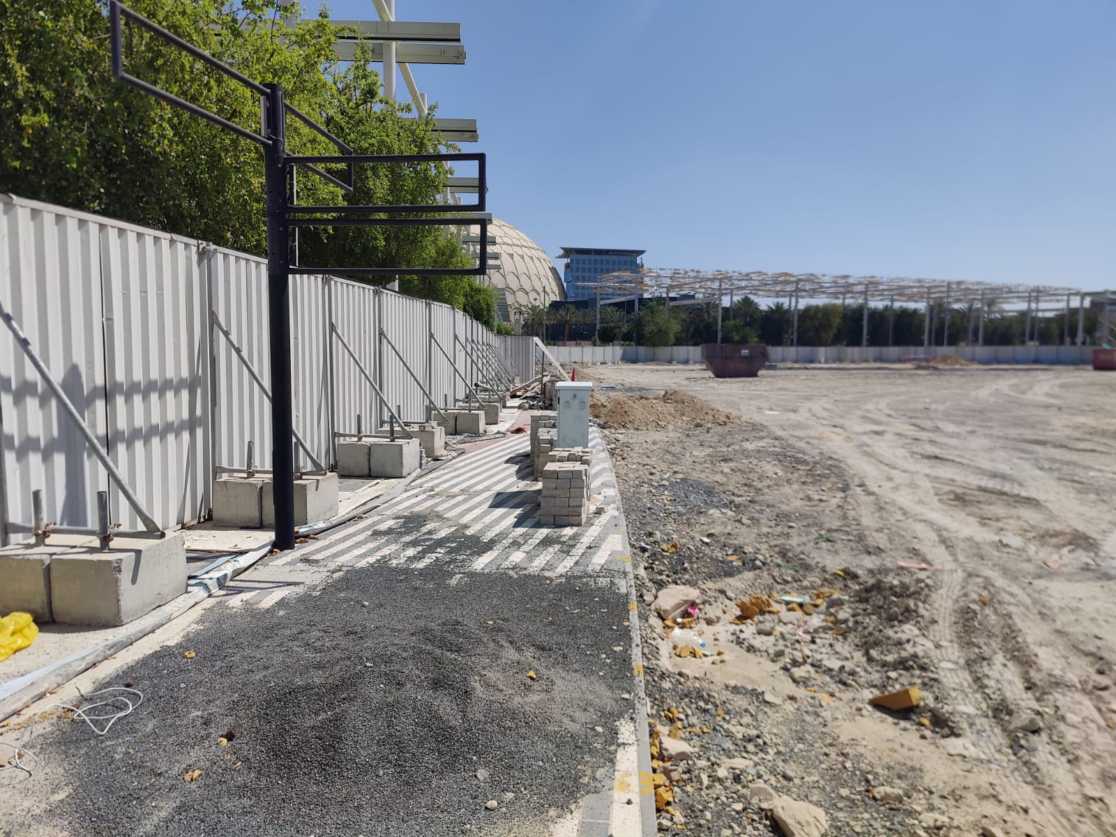 Poland Pavilion site view showing graded ground and hoarding with Expo City buildings