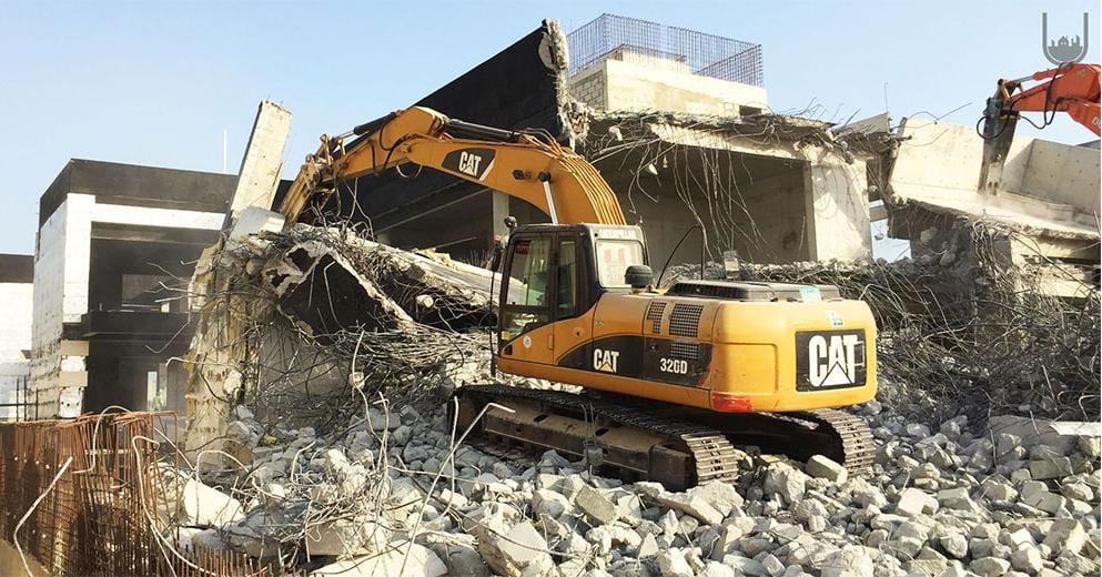 USF excavator performing structural demolition amid reinforced concrete debris