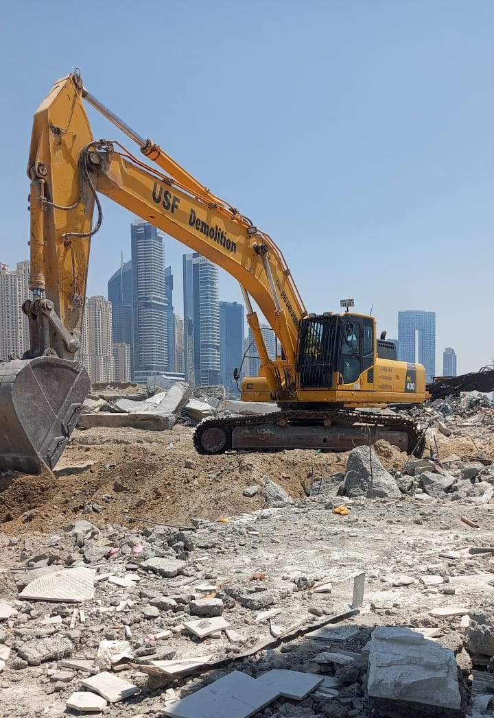 USF Demolition Komatsu excavator on cleared Zero Gravity site with Dubai Marina towers in background after structural demolition
