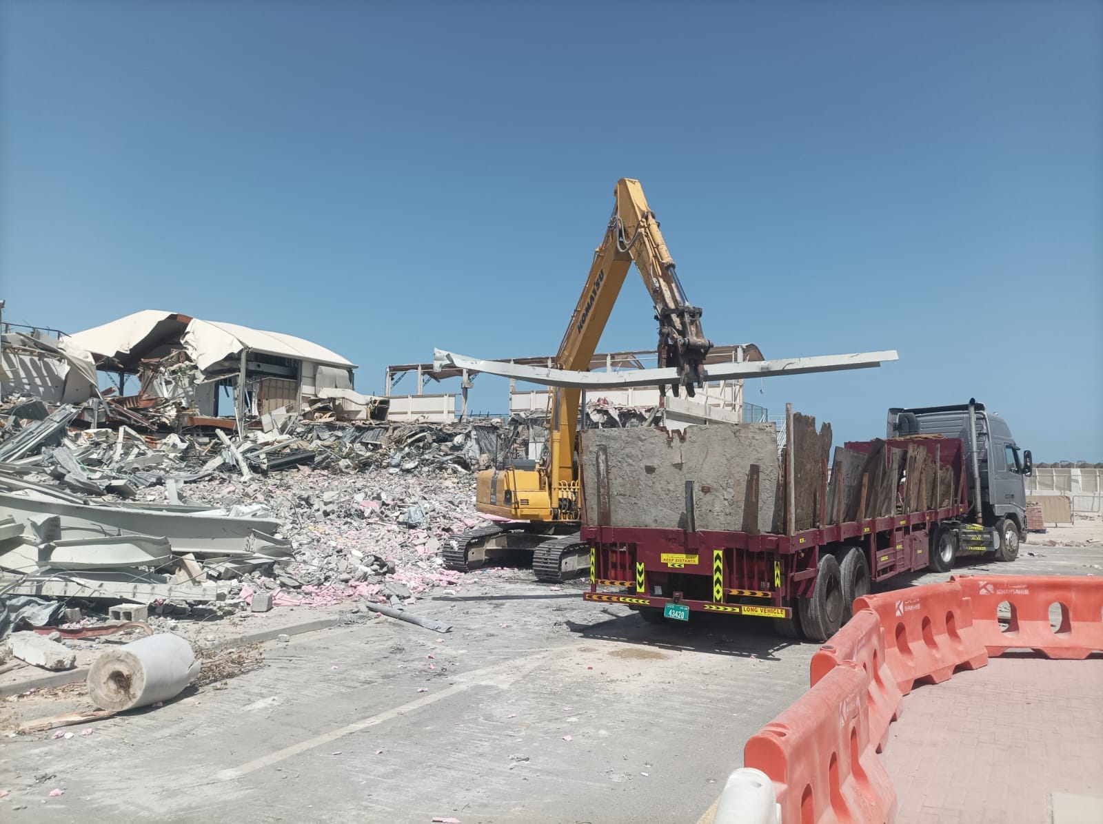 Komatsu excavator loading large concrete slab onto long-vehicle trailer for waste haulage at Zero Gravity demolition site Dubai Marina